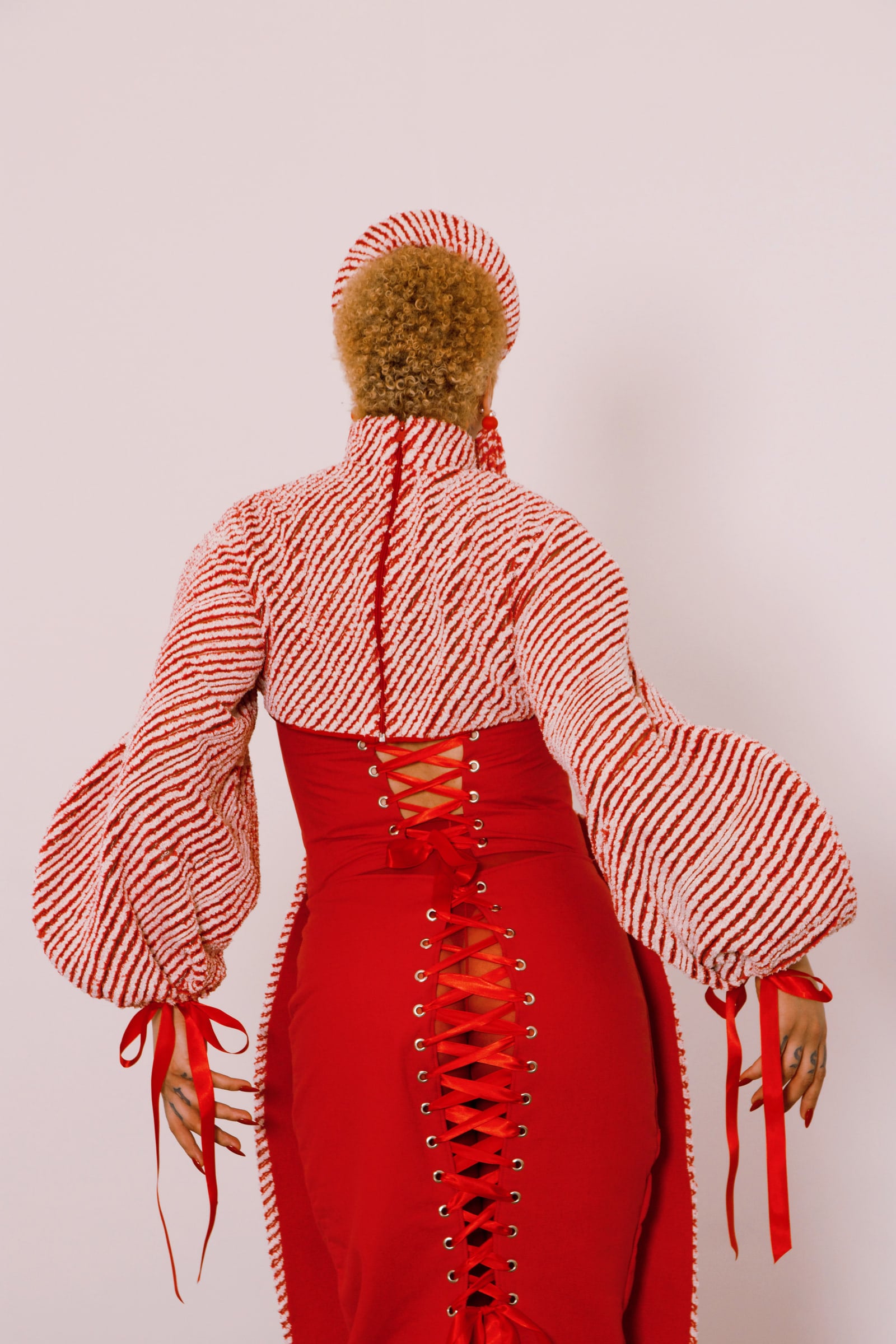Back view of the dress, with red cross lacing down the centre, voluminous striped sleeves and ribbons at the cuffs.