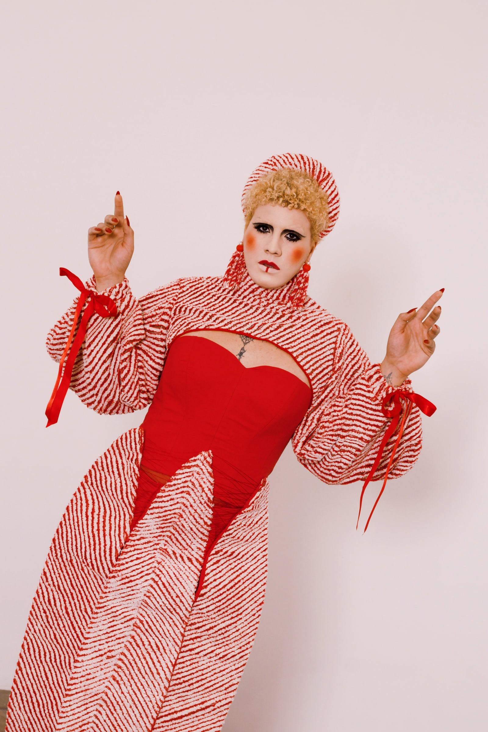 Model leaning forward with hands raised, showing the volume of the sleeves, the red ribbons and the striped panels of the skirt.