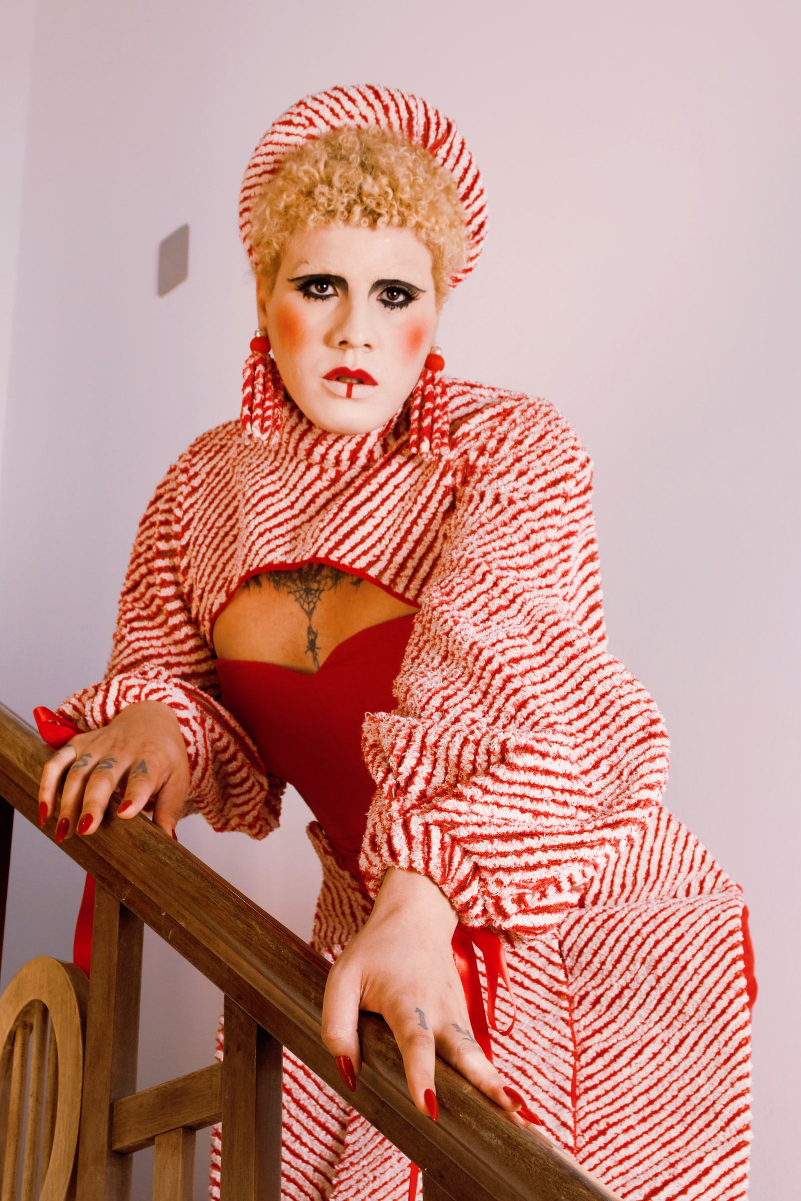 Model with both hands on a wooden handrail. The striped piece wraps the neck and shoulders over a red dress.